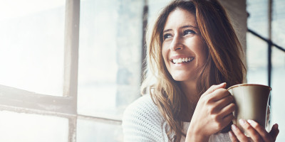 Woman smiling in the sun with a cup of coffee or tea