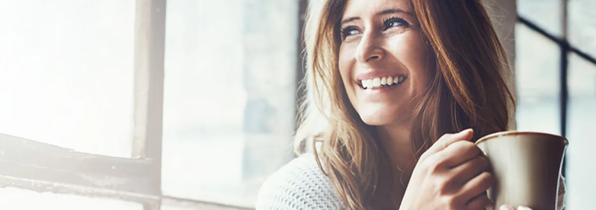 Woman smiling in the sun with a cup of coffee or tea