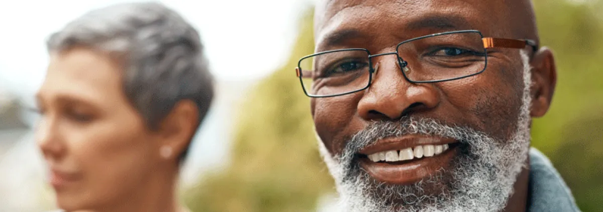 Man smiling at camera with his spouse in the background