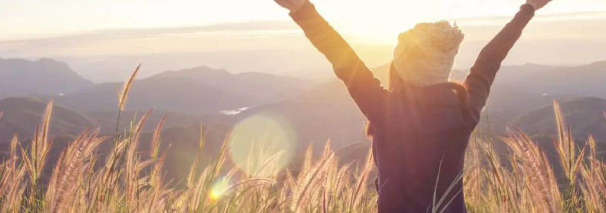 Woman in a wheat field with arms raised high
