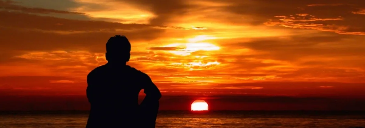 man sitting by the ocean at sunset
