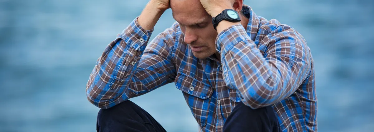 Man by the water with head in hands